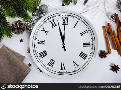 Christmas table place setting - white table with blue plate, white fork and knife, decorated sprig of mistletoe and christmas pine branches. New Year Clock Symbol.