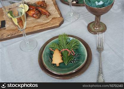 Christmas table setting. Brown-green vintage plates, vintage fork, spruce branch and gingerbread tree, fried meat on a wooden tray, gray tablecloth and stars from orange peels.