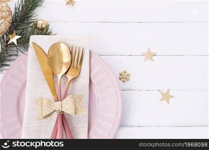 Christmas table setting in white-pink-gold colors. pink plate, cutlery with gold bow, fir branches, snowflakes and stars.