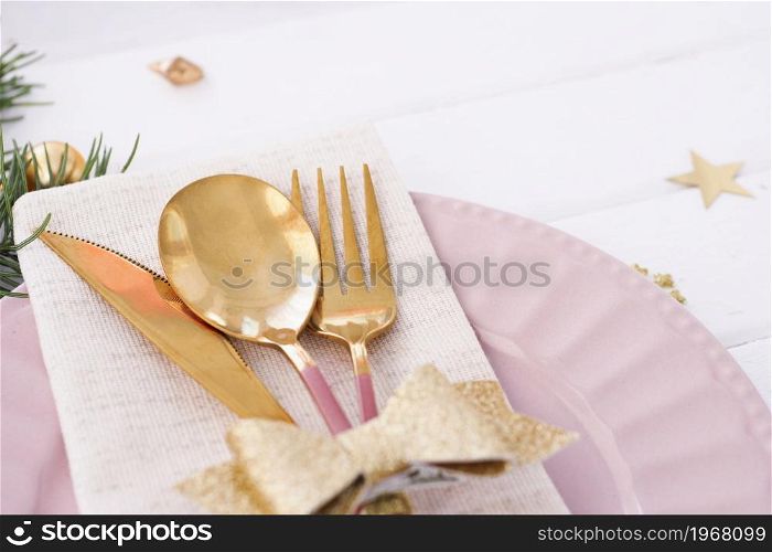 Christmas table setting. pink plate, cutlery with gold bow, fir branches and stars.