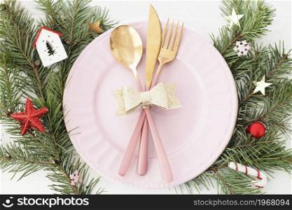 Christmas table setting . pink plate, cutlery with gold bow, fir branches, snowflakes and stars.
