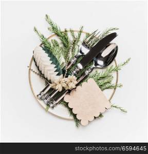 Christmas table setting . Plate with fir branches , cutlery and festive holiday decoration: pine cone and tag on white background, top view