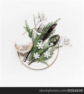 Christmas table setting . Plate with fir branches , cutlery and festive holiday decoration: ball and little snowflakes on white background, top view