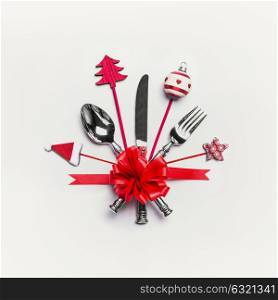 Christmas table setting with cutlery, red ribbon and decoration: Santa hat, Christmas tree, bauble and star on white desk background. Layout for holiday greeting card, festive, dinner invitation