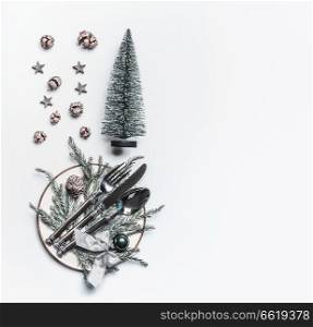 Christmas table setting with decorative fir tree,cones, plate and cutlery on white background, top view. Festive table decoration for Christmas dinner, flat lay