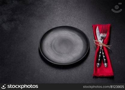 Christmas table setting with empty black ceramic plate, fir tree branch and black accessories on black stone background. Christmas table setting with empty black ceramic plate, fir tree and black accessories