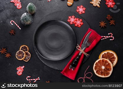 Christmas table setting with empty black ceramic plate, fir tree branch and black accessories on black stone background. Christmas table setting with empty black ceramic plate, fir tree and black accessories