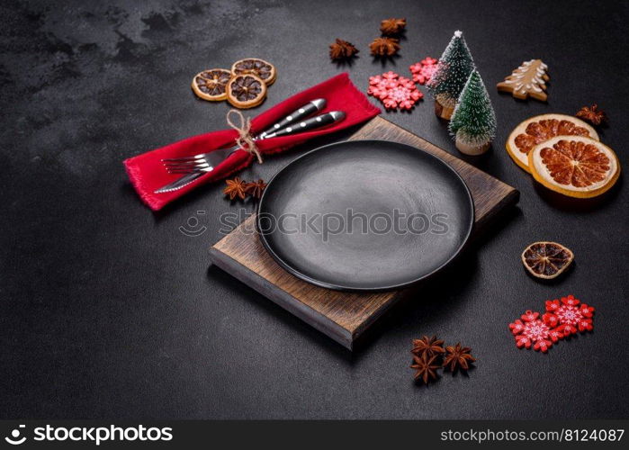 Christmas table setting with empty black ceramic plate, fir tree branch and black accessories on black stone background. Christmas table setting with empty black ceramic plate, fir tree and black accessories