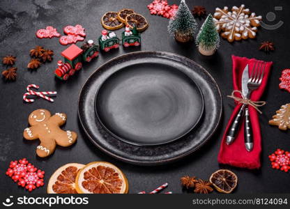 Christmas table setting with empty black ceramic plate, fir tree branch and black accessories on black stone background. Christmas table setting with empty black ceramic plate, fir tree and black accessories