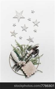 Christmas table setting with plates, cutlery , fir branches, stars and tags on white background, top view, flat lay. Holiday concept