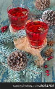 Christmas table: two glasses of red hot mulled wine ore compote (stewed fruit) with spices and cowberries surrounded by fir branches and cones