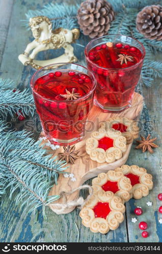Christmas table - two glasses of red hot mulled wine with spices and cowberries and cookies with jam, surrounded by fir branches and cones
