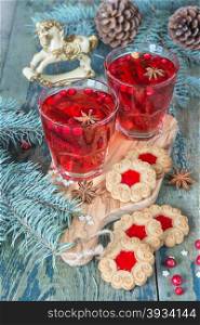 Christmas table - two glasses of red hot mulled wine with spices and cowberries and cookies with jam, surrounded by fir branches and cones