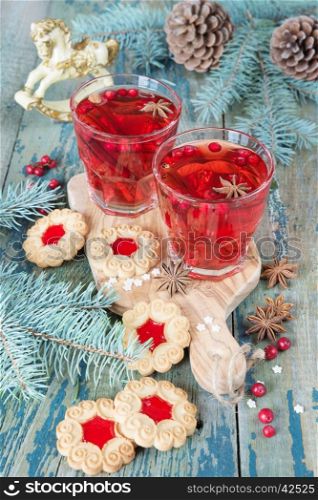 Christmas table: two glasses of red hot mulled wine with spices and cowberries and cookies with jam, surrounded by fir branches and cones