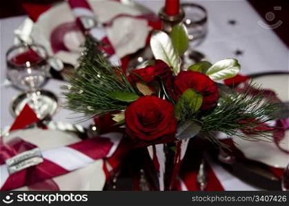 Christmas table with red decoration, napkins, roses, silver, christmas tree and candles
