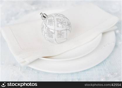 Christmas table with white plates, linen napkin, and a beautiful Christmas ball