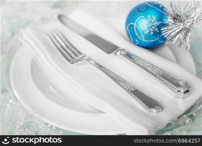 Christmas table with white plates, linen napkin, silver knife and fork and a beautiful blue Christmas ball