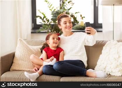 christmas, technology and family concept - happy mother and little daughter taking selfie by smartphone at home. family taking selfie by smartphone at home