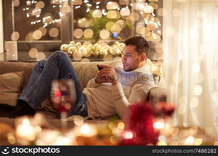 christmas, technology and holidays concept - man with smartphone texting message at home. man with smartphone at home for christmas