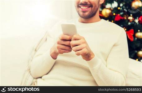 christmas, technology, people and holidays concept - close up of smiling man with smartphone at home. smiling man with smartphone at home for christmas