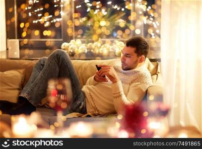 christmas, technology, people and holidays concept - man with smartphone texting message at home. man with smartphone at home at christmas eve