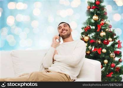 christmas, technology, people and holidays concept - smiling man calling on smartphone over blue holidays lights background