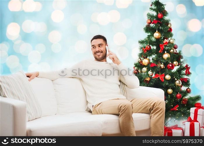 christmas, technology, people and holidays concept - smiling man calling on smartphone over blue holidays lights background