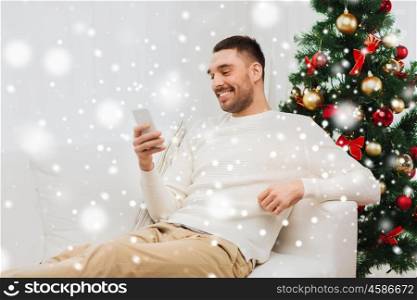 christmas, technology, people and holidays concept - smiling man with smartphone texting message at home