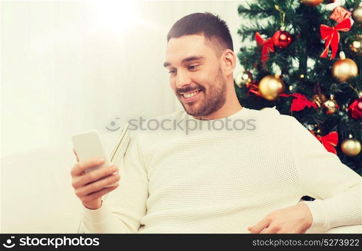 christmas, technology, people and holidays concept - smiling man with smartphone texting message at home. smiling man with smartphone at home for christmas