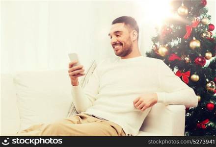 christmas, technology, people and holidays concept - smiling man with smartphone texting message at home. smiling man with smartphone at home for christmas