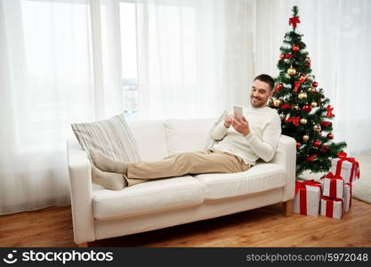 christmas, technology, people and holidays concept - smiling man with smartphone texting message at home