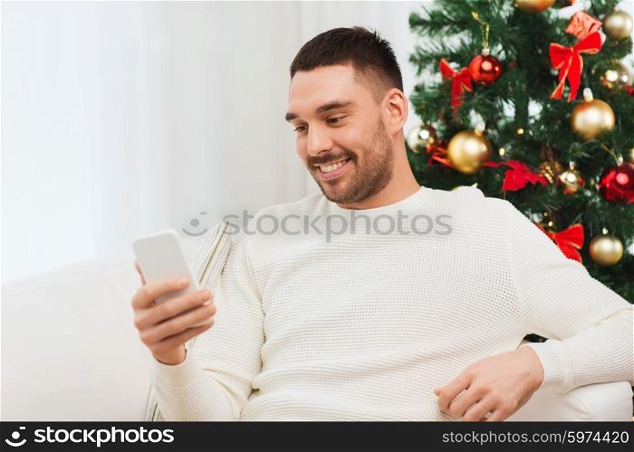 christmas, technology, people and holidays concept - smiling man with smartphone texting message at home