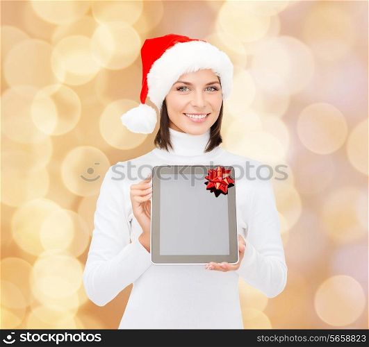 christmas, technology, present and people concept - smiling woman in santa helper hat with blank screen tablet pc computer over beige lights background
