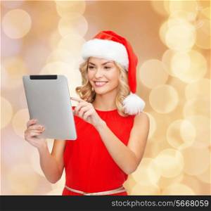 christmas, technology, present and people concept - smiling woman in santa helper hat with tablet pc computer over beige lights background