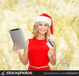 christmas, technology, shopping and people concept - smiling woman in santa helper hat with tablet pc computer and credit card over yellow lights background