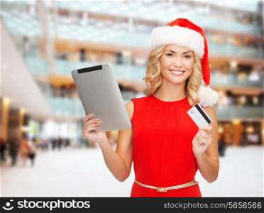 christmas, technology, shopping and people concept - smiling woman in santa helper hat with tablet pc computer and credit card over lights background