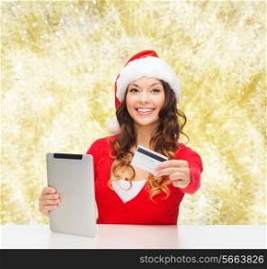 christmas, technology, shopping and people concept - smiling woman in santa helper hat with tablet pc computer and credit card over yellow lights background