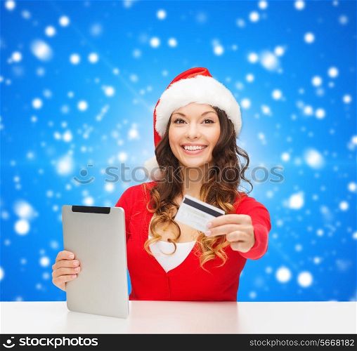 christmas, technology, shopping and people concept - smiling woman in santa helper hat with tablet pc computer and credit card over blue snowing background
