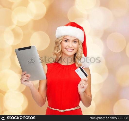 christmas, technology, shopping and people concept - smiling woman in santa helper hat with tablet pc computer and credit card over beige lights background