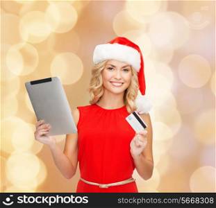 christmas, technology, shopping and people concept - smiling woman in santa helper hat with tablet pc computer and credit card over beige lights background