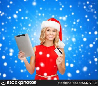 christmas, technology, shopping and people concept - smiling woman in santa helper hat with tablet pc computer and credit card over blue lights background