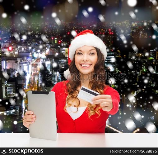 christmas, technology, shopping and people concept - smiling woman in santa helper hat with tablet pc computer and credit card over snowy night city background