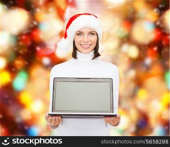 christmas, technology, winter holidays and people concept - smiling woman in santa helper hat with blank screen laptop computer over red lights background