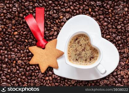 Christmas time concept. Gingerbread cookie star shaped, white cup with saucer in shape of heart on coffee beans background