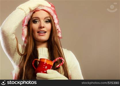 Christmas time concept. Pretty shocked woman in fur cap hat holding red mug with beverage and sweet candy cane.. Christmas girl with mug and cane.