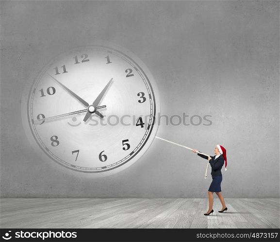 Christmas time is coming. Woman in Santa hat pulling clock with rope