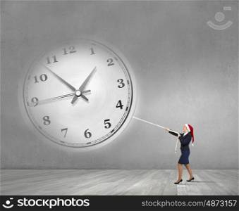 Christmas time is coming. Woman in Santa hat pulling clock with rope