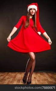 Christmas time. Pretty female wearing santa claus hat on grey background. Studio shot.