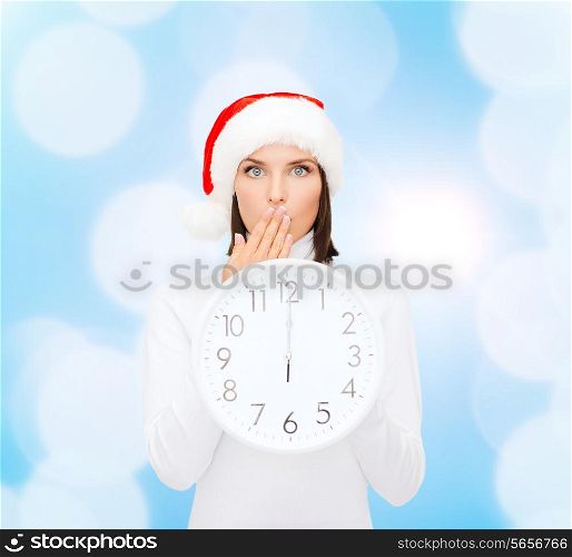 christmas, time, winter and people concept - smiling woman in santa helper hat with clock showing 12 over blue lights background