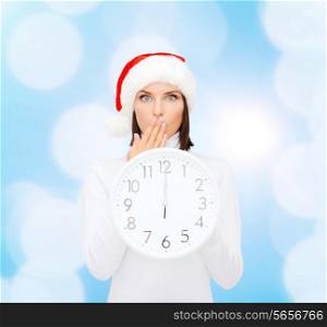 christmas, time, winter and people concept - smiling woman in santa helper hat with clock showing 12 over blue lights background